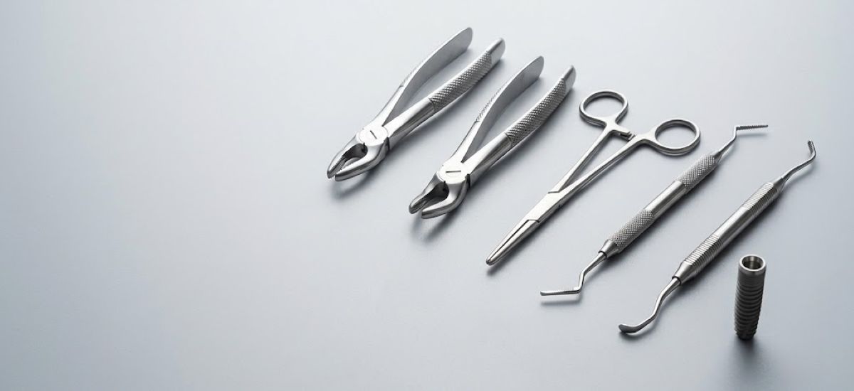 Extraction forceps, hemostat, dental tools, and a one-piece implant laid out on a gray surface
